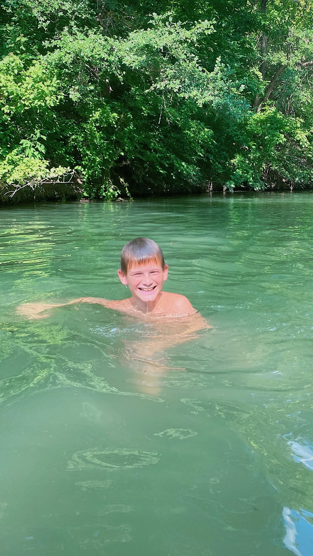 Boy swimming in Geronimo Creek with the bluish-green spring-fed water
